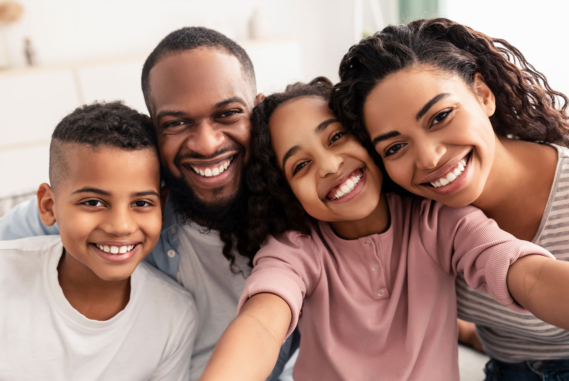 Family of four posing for a selfie, with the father taking the photo and all smiling.