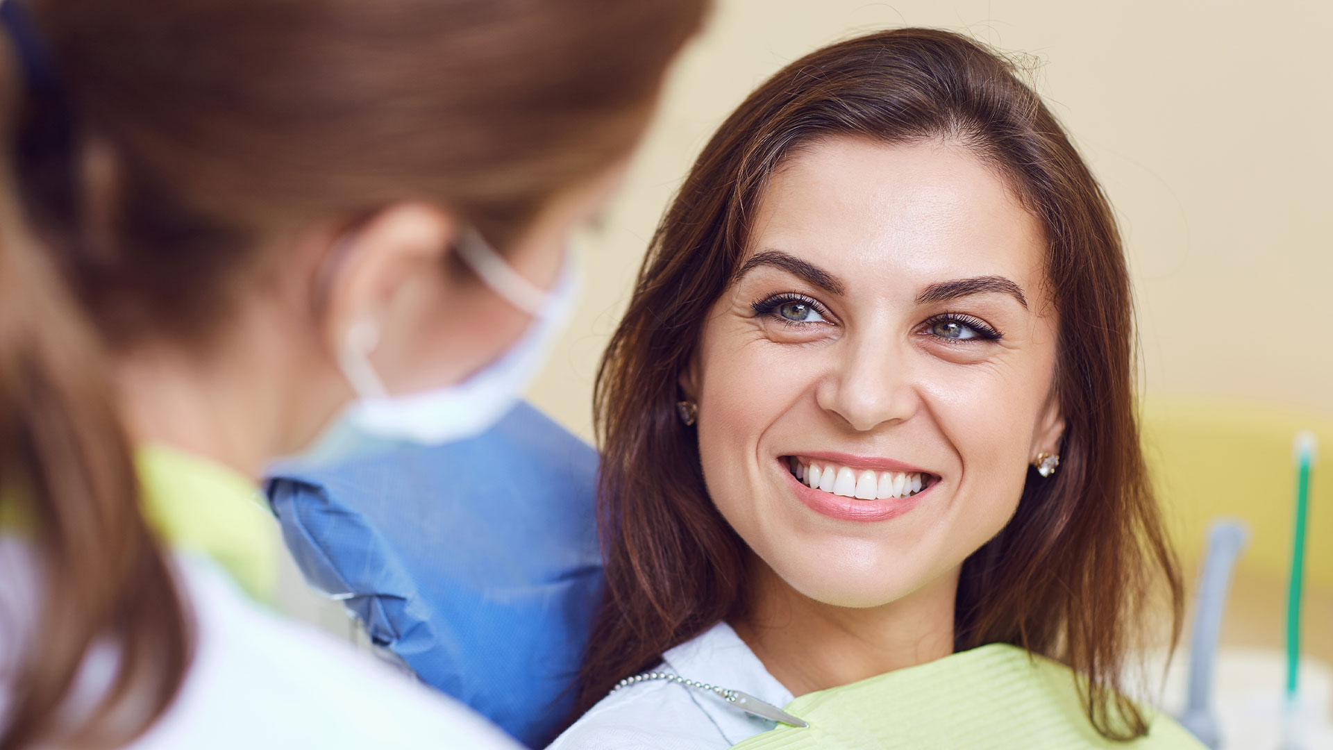 A dental hygienist is smiling at a patient, both in a dental office setting.