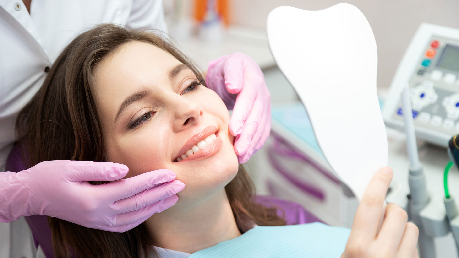 The image shows a woman sitting in a dental chair, receiving dental care from a professional wearing gloves and a face mask.