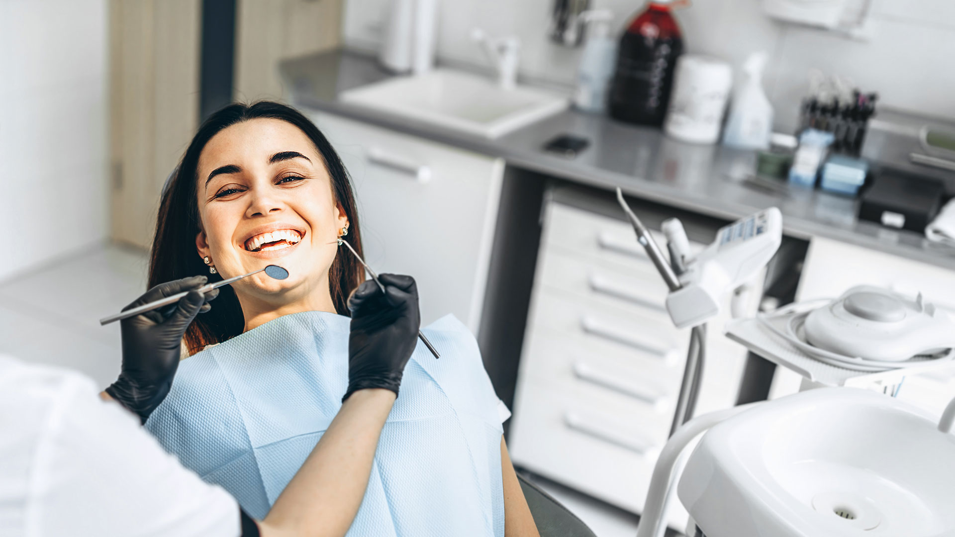 A smiling woman in a dental office, sitting in the chair with her mouth open, receiving dental care.