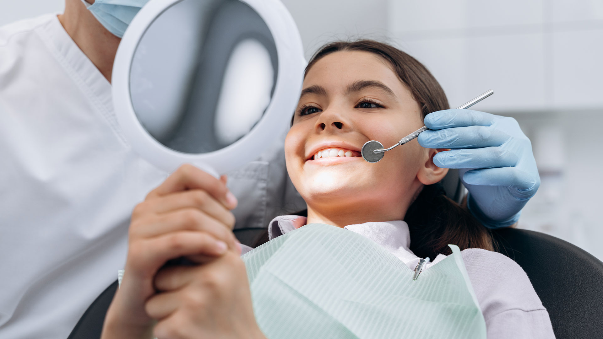 A dental professional is examining a patient s teeth, with the patient smiling and wearing a surgical mask.