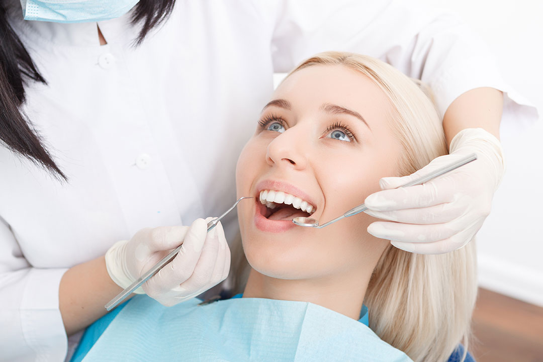 A woman receiving dental care from a dentist, with the dentist using a drill on her teeth.