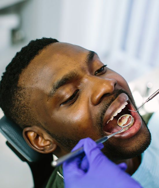 A man with a toothy grin is sitting in a dental chair, receiving dental care.