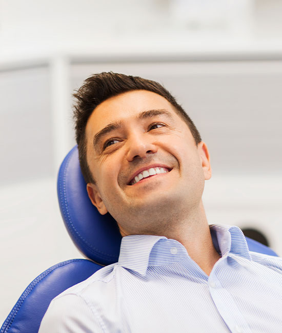 A man is seated in a dental chair, smiling broadly, with his eyes closed.