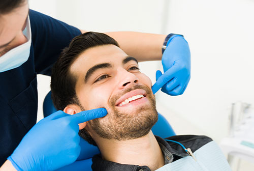 A dental professional is performing a teeth cleaning procedure on a smiling man, who appears relaxed and comfortable.