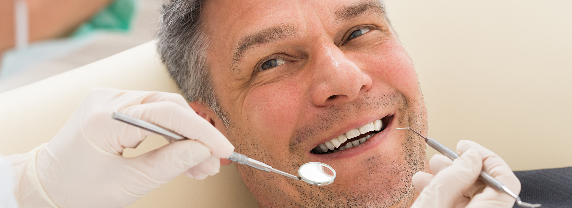 The image shows a man sitting in a dental chair, receiving dental care with a smile on his face.