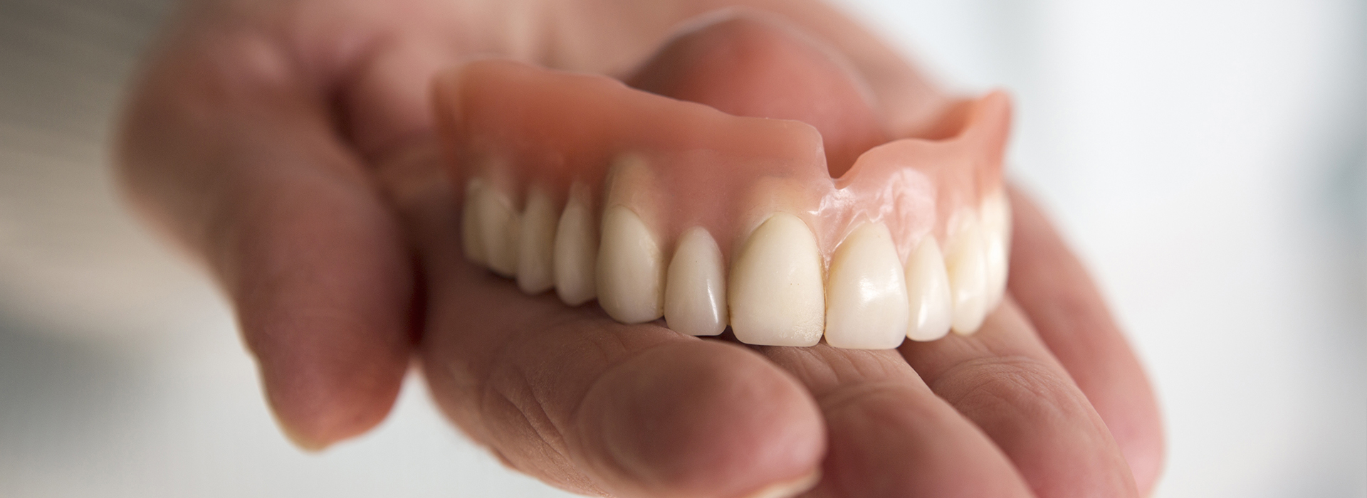 The image shows a person s hand holding a set of dentures.