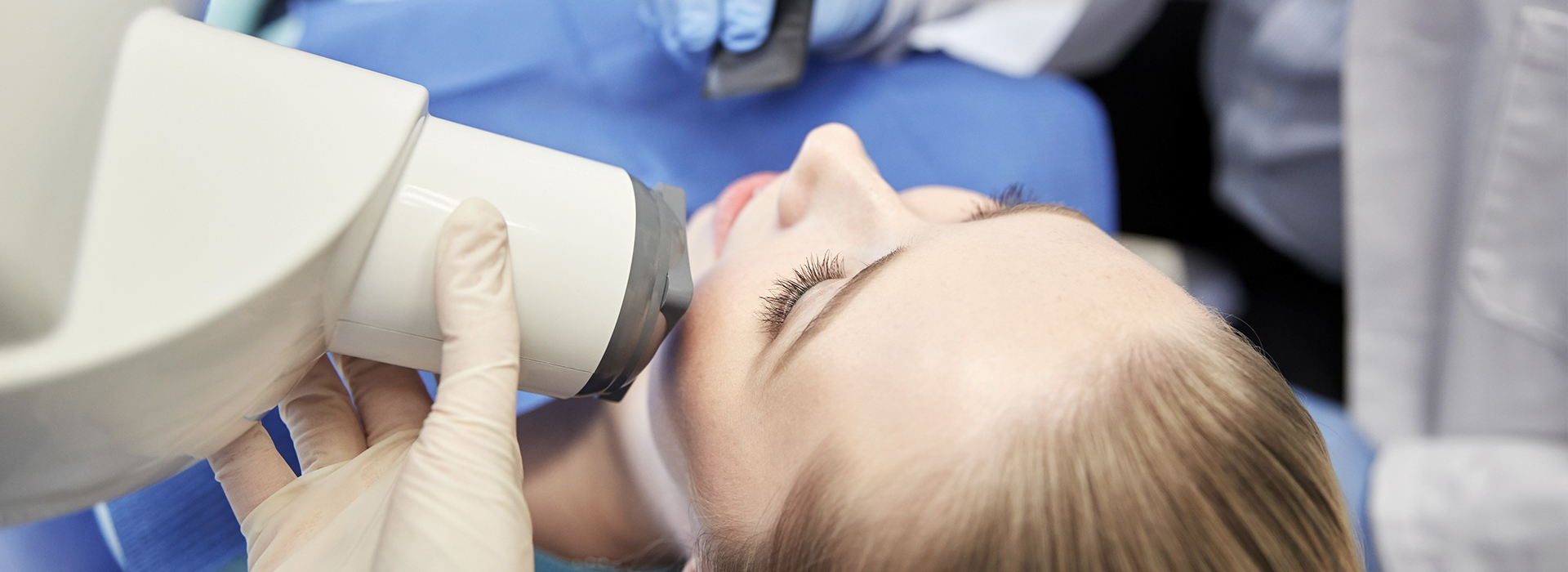 A person receiving a dental examination, with a dentist using a magnifying device to inspect their teeth.