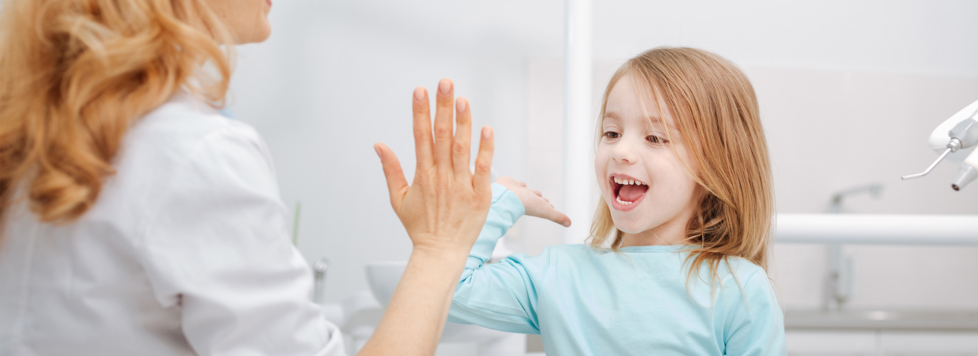 A woman and a child in a dental office, with the woman extending her hand towards the child.