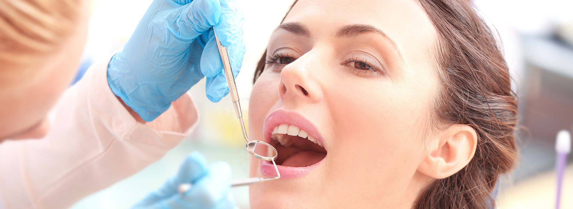 The image depicts a woman having her teeth cleaned by a dental professional, with the professional using a tool to remove plaque or debris from the woman s teeth.