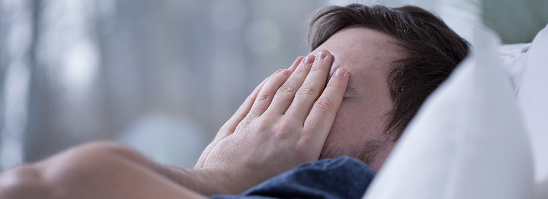 The image shows a person lying in bed with their hands covering their face, appearing to be asleep or resting.