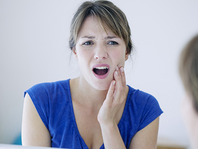 An adult female with a concerned expression, holding her hand to her mouth while looking into a mirror.