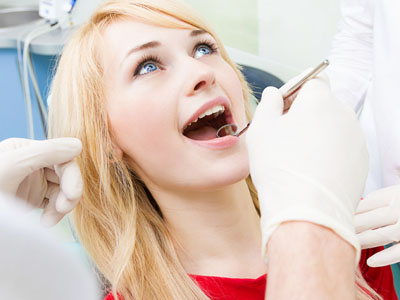 A woman receiving dental care from a professional, with one hand holding her mouth open and the other hand resting on her chin.