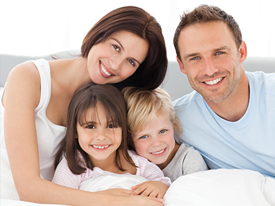 A family of four, including two adults and two children, posing for a photo in a bedroom setting.