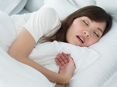 A woman sleeping peacefully in bed with her eyes closed and a slight smile on her face.