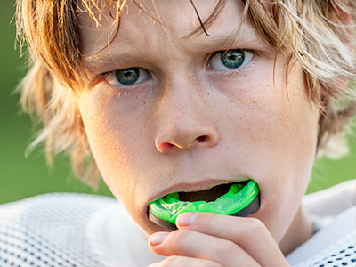 A young male athlete with a mouthguard, brushing his teeth.